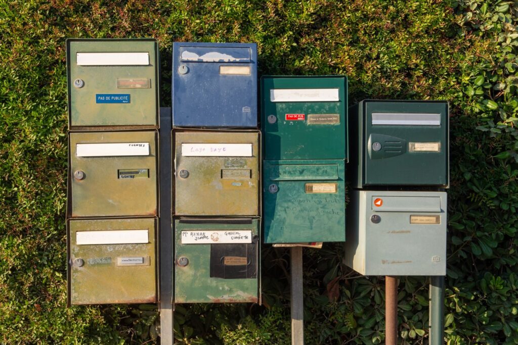 A collection of vintage metal mailboxes on posts against a hedge backdrop.